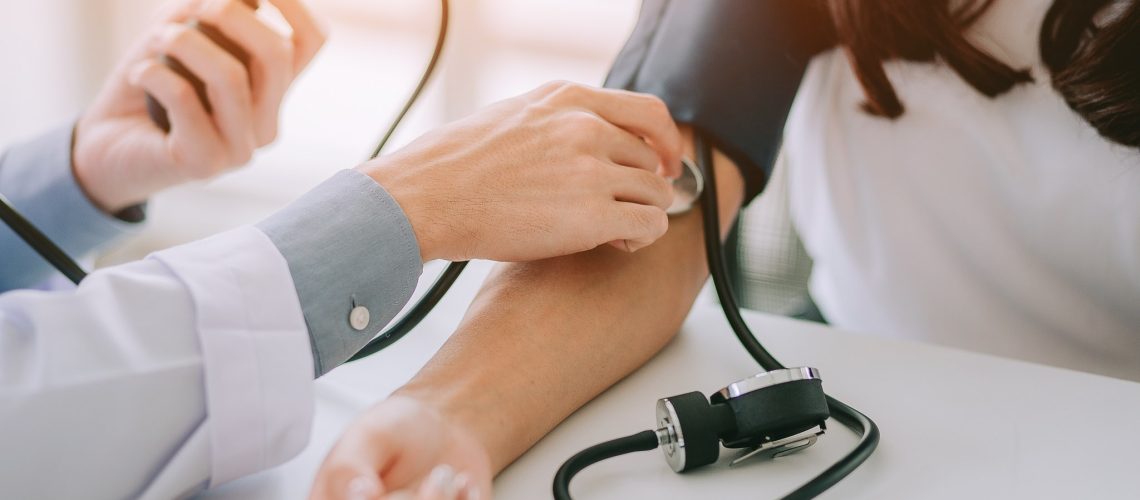 Doctor using sphygmomanometer with stethoscope checking blood pressure to a patient in the hospital.